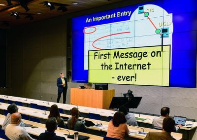Leonard Kleinrock next to his presentation slide that reads, "First message on the internet - ever!"